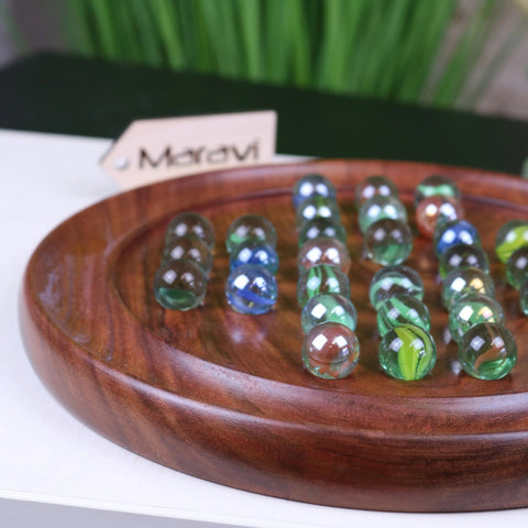 A polished jajur wooden solitaire game board with colorful translucent marbles arranged in rows for playing solitaire game