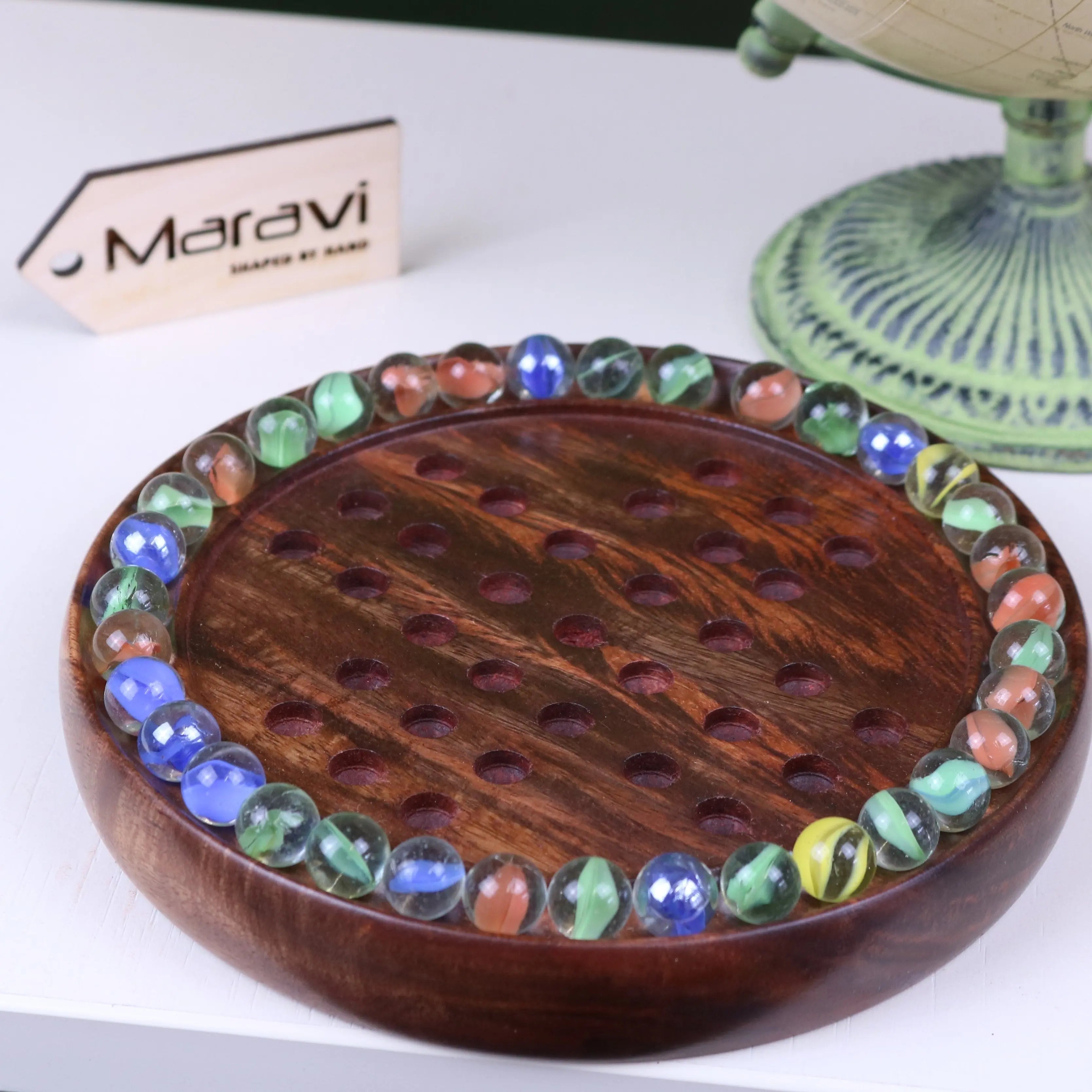 Round wooden board of jajur wooden solitaire game with colorful glass marbles arranged around the edge