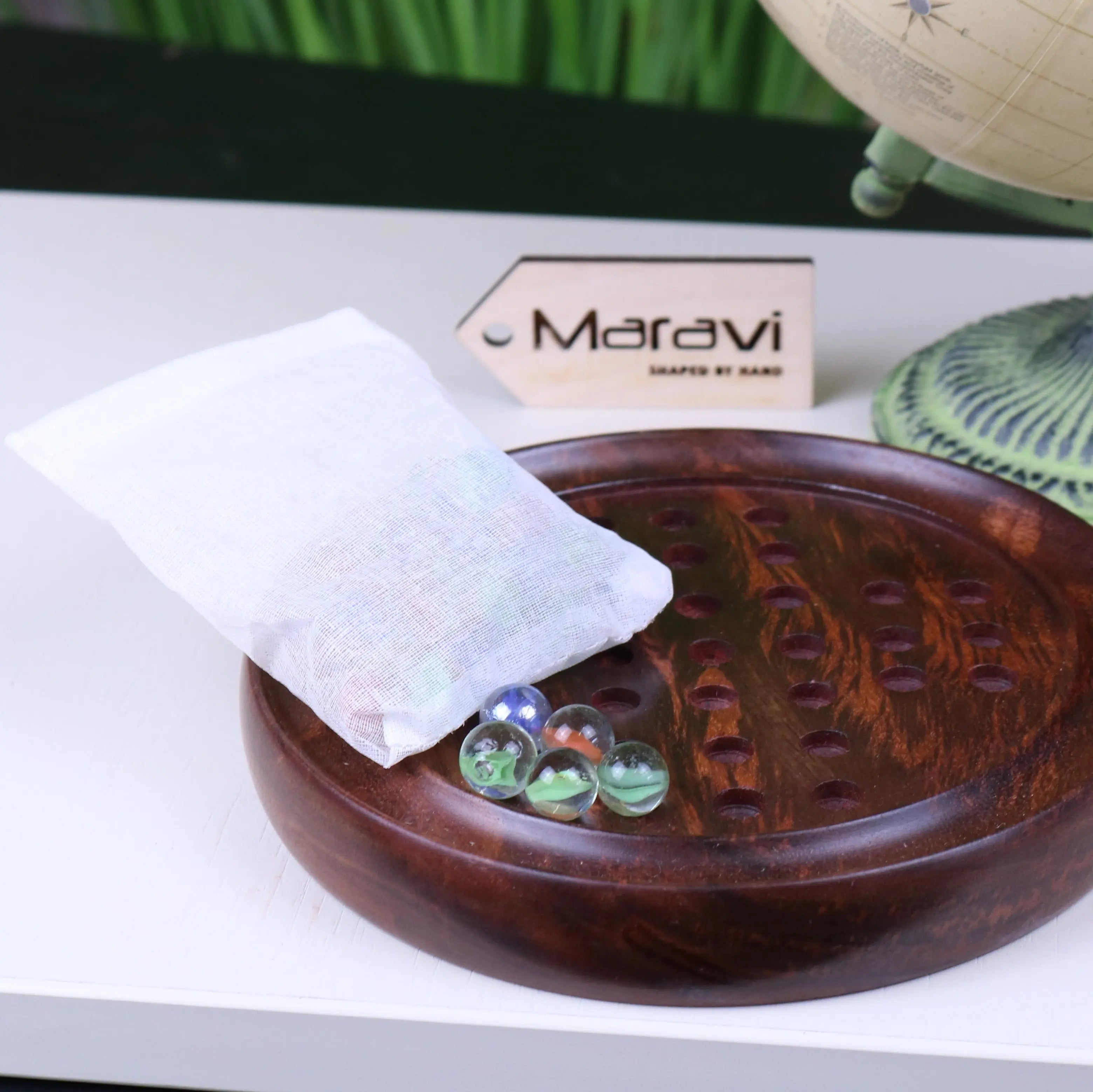 White mesh bag filled with colorful glass marbles resting on dark wooden board for jajur wooden solitaire game