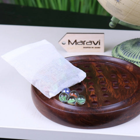 White mesh bag filled with colorful glass marbles resting on dark wooden board for jajur wooden solitaire game