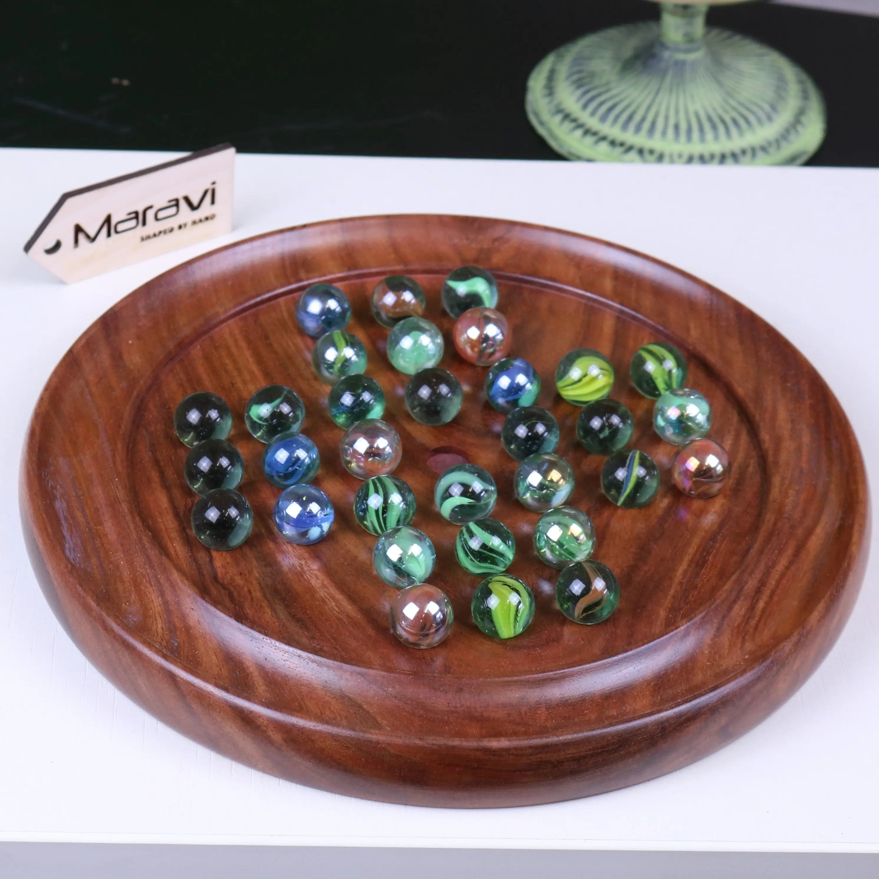 A jajur wooden solitaire game with a round dark brown board and colorful glass marbles for classic solitaire game fun