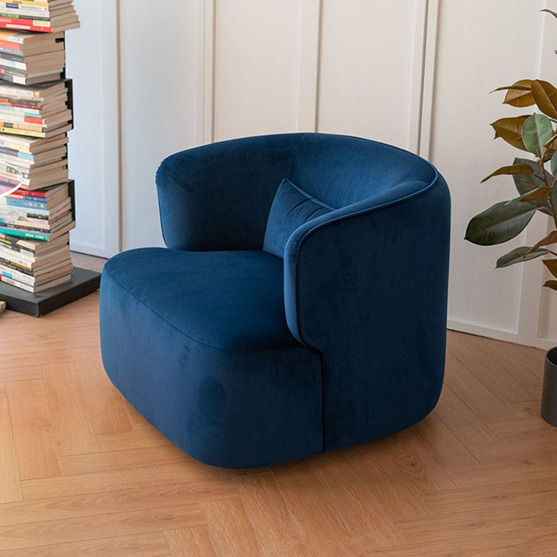 A plush deep blue velvet jaotoo armchair with a modern rounded design and matching cushion perfect for cozy lounging