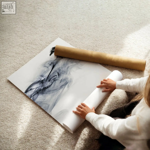 A large abstract black and gray ink wash landscape art print partially rolled up by hands on white canvas
