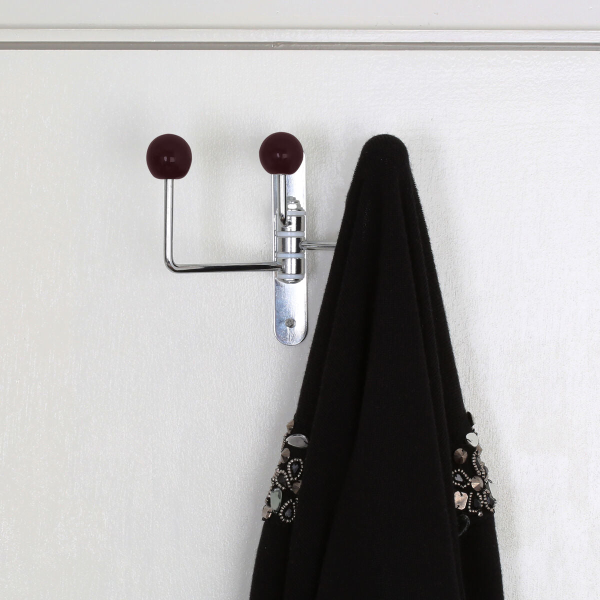 Chrome-plated double hook with jaxen purple ceramic balls holding a black garment on white wall