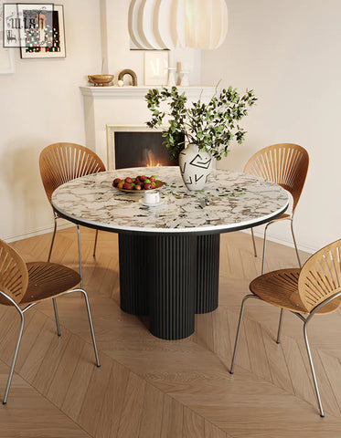 Jean round dining table with white marble top and black ribbed pedestal base featuring a white vase with greenery