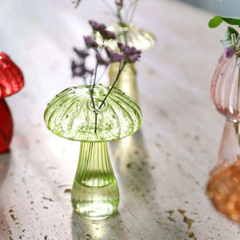 A translucent green glass jelly mushroom vase with ribbed stem and textured cap holding delicate purple flowers