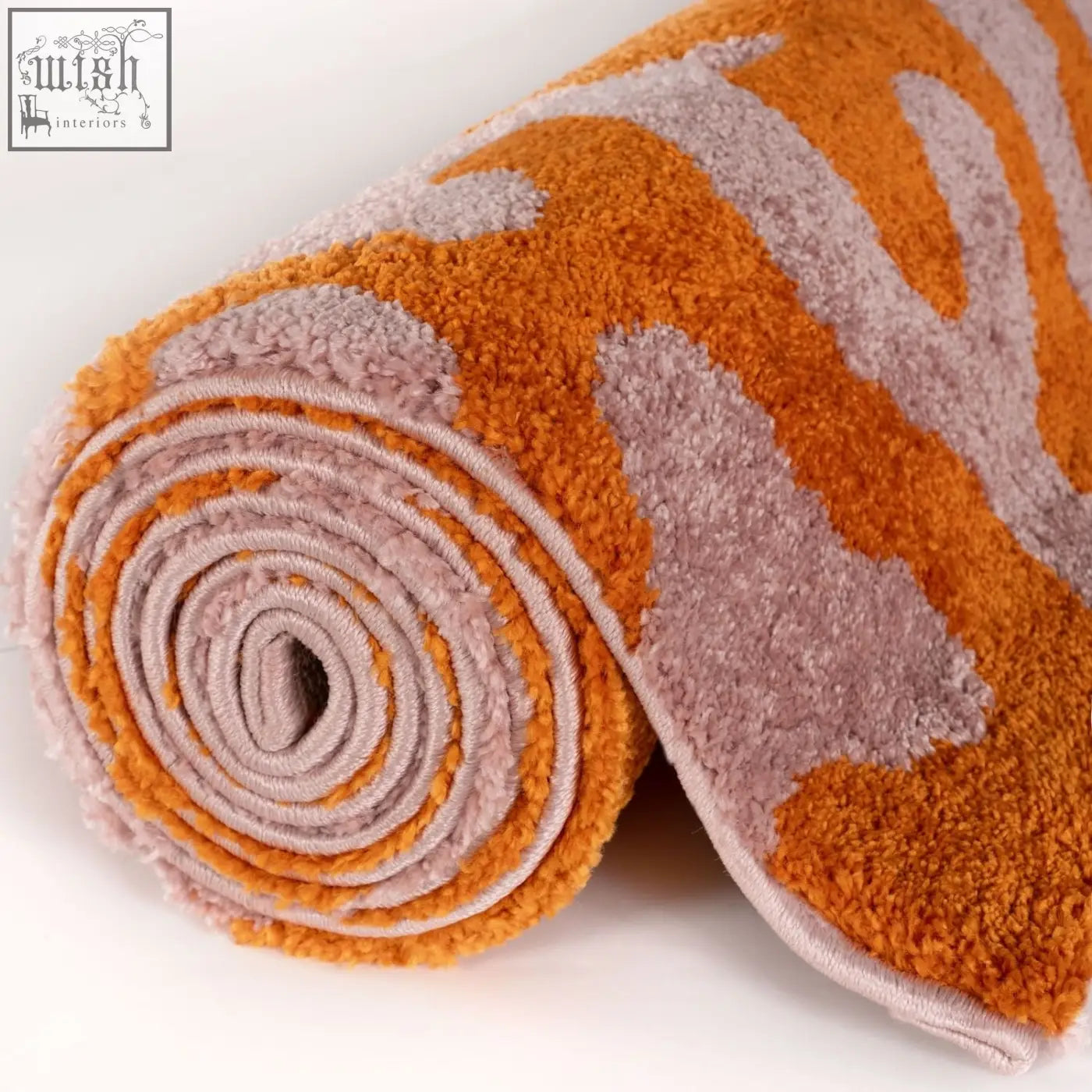 A plush rolled bath mat with soft textured fibers in a bold joli doodle orange and muted pink abstract pattern