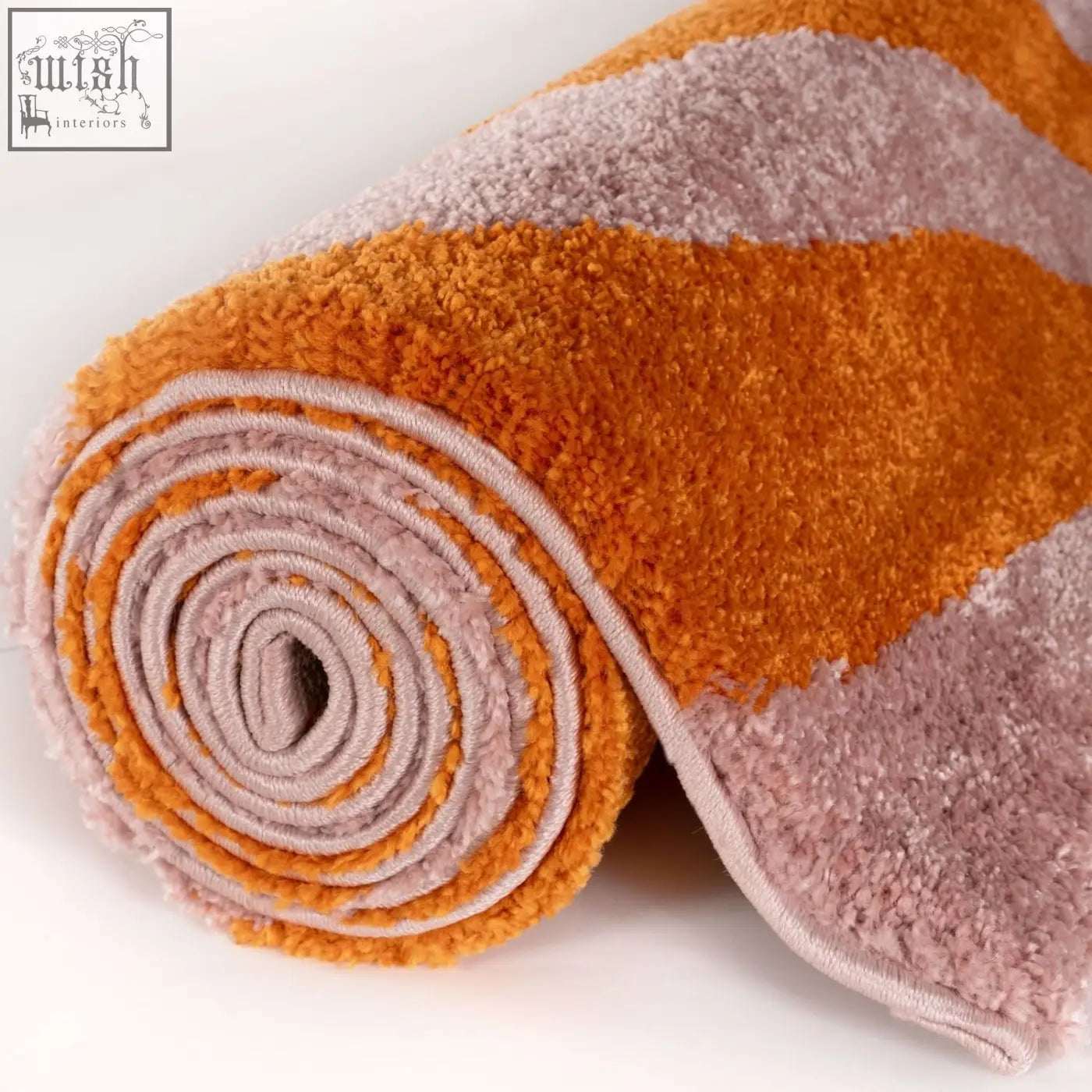 A plush rolled bath mat with a flowing striped pattern in warm orange and soft pink from joli striped orange collection