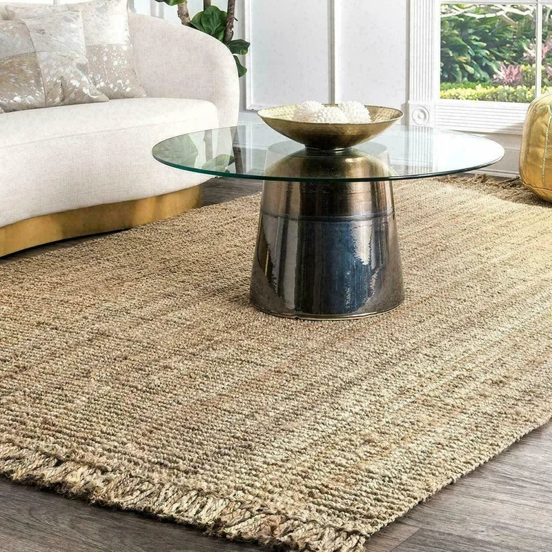 A round glass-top coffee table with a brushed gold metallic base paired with a Joto rug underneath