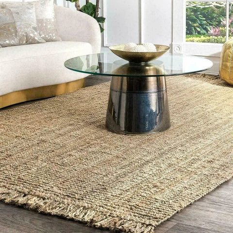 A round glass-top coffee table with a brushed gold metallic base paired with a Joto rug underneath
