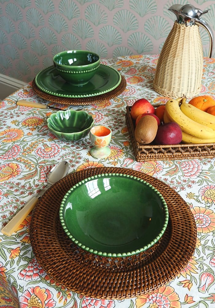 Green ceramic bowl with beaded rim on brown woven placemat featuring juliettes floral tablecloth table linen