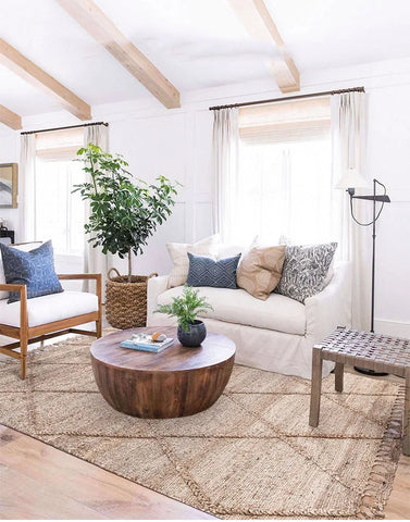 Round wooden coffee table with natural finish and visible grain paired with junya rug for cozy living room setup