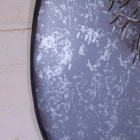 A round distressed gray mirror with a dark metal frame perfect as kailora tree metal garden wall art or garden wall decor