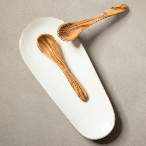 Two olive wood spoons on a kara mango wood small oval serving dish with white ceramic handcrafted edge