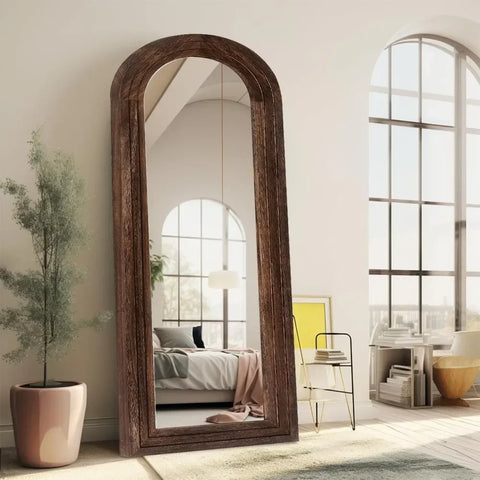 A tall kayo mirror with a rustic dark wood frame and arched design stands against the wall