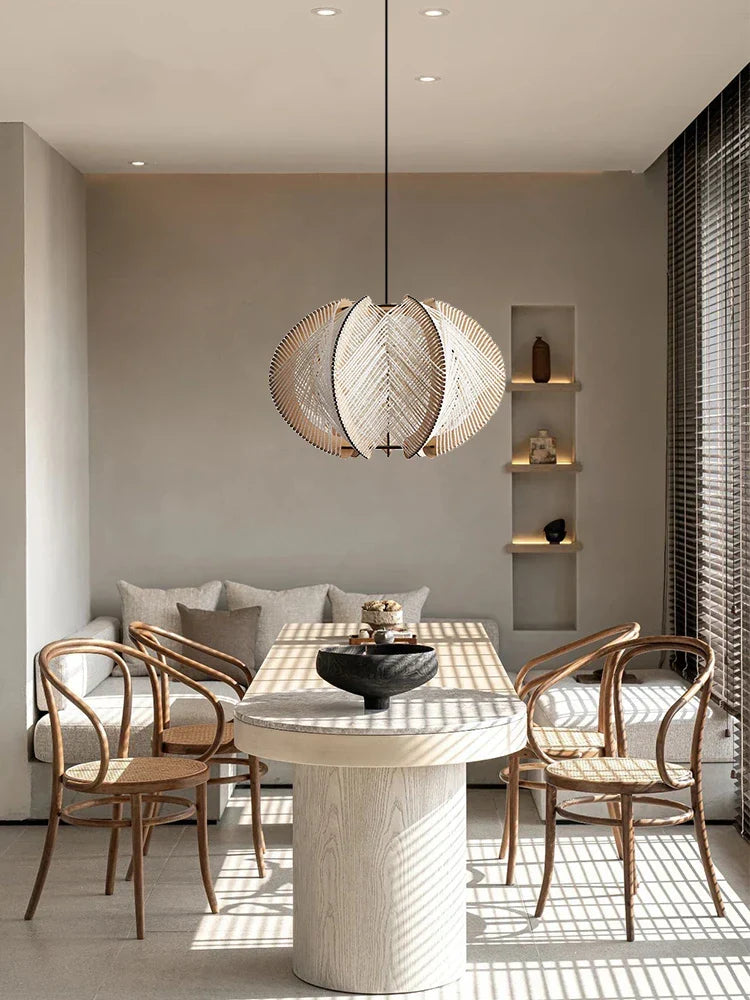 A modern kazaru light pendant with a woven leaf-shaped design in natural wood hanging above a dining table