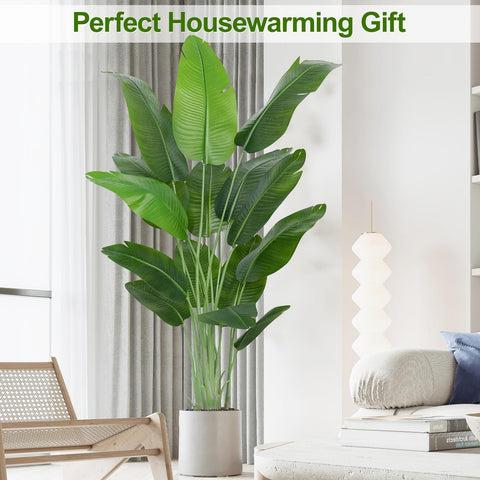 A tall lush green artificial bird of paradise plant banana tree with broad leaves in a white ceramic pot for indoor use