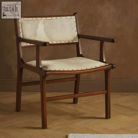 A rustic kendari wood dining chair with cream upholstery and brass nailhead trim made of teak wood