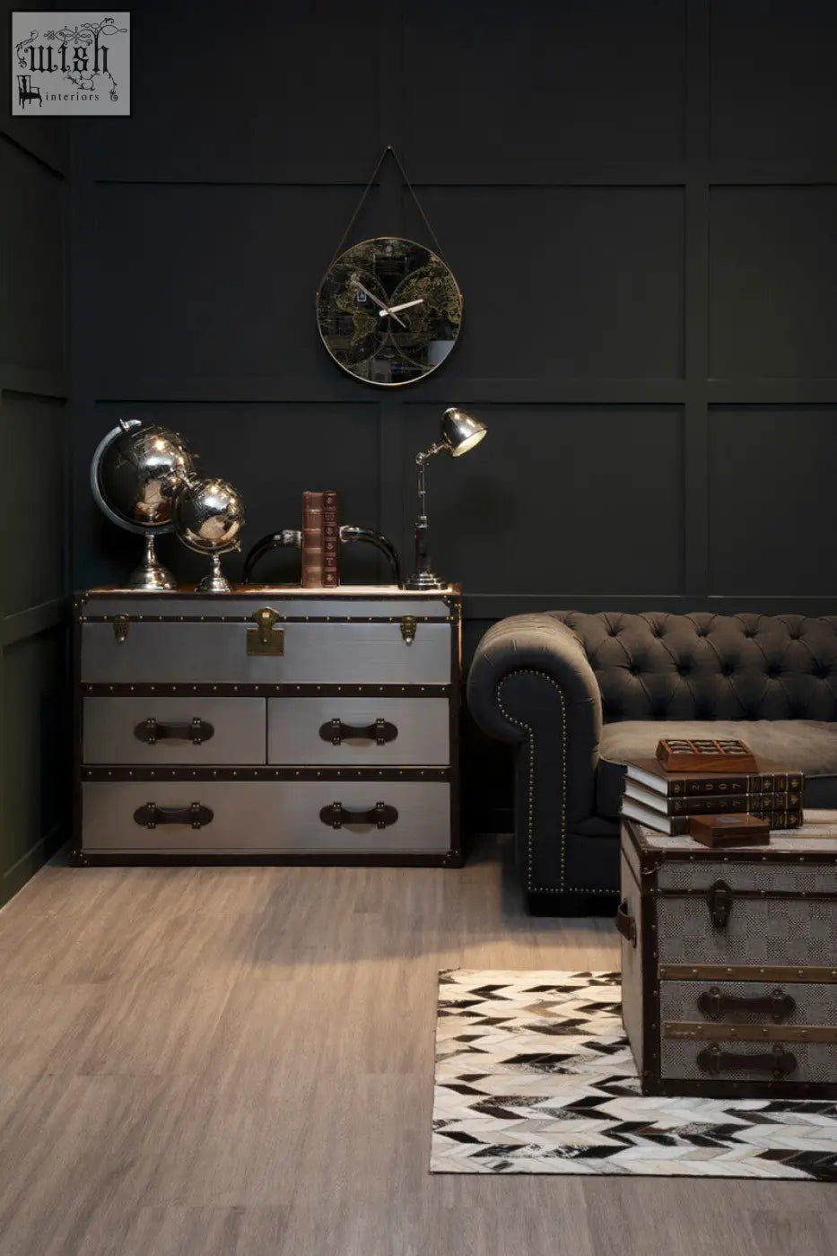 Silver and black vintage-style trunk with brass hardware next to kensington townhouse brown and white cowhide cabinet