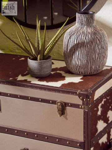 A tall rounded ceramic vase with a textured black and white striped pattern next to a kensington townhouse brown white cowhide cabinet