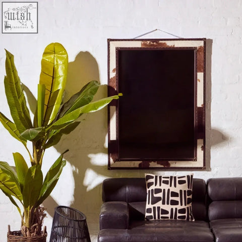 Rustic-framed genuine cowhide wall mirror with white genuine cowhide distressed metal border above dark leather sofa