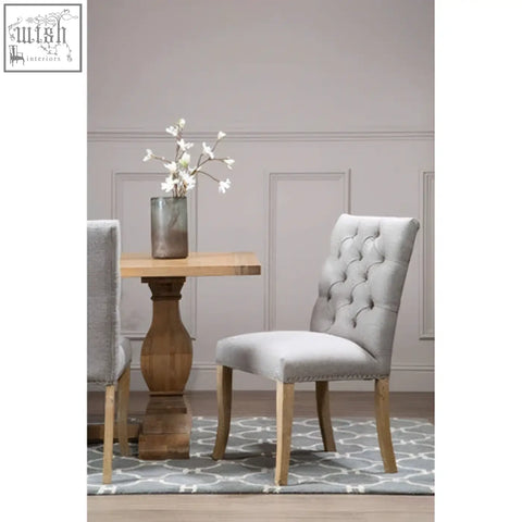 Light gray tufted linen dining chair with wooden legs and nailhead trim perfect for a grey linen dining room setup