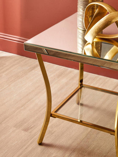 Kensington townhouse mirror side table with gold legs features a glass top, curved iron legs, and a lower shelf