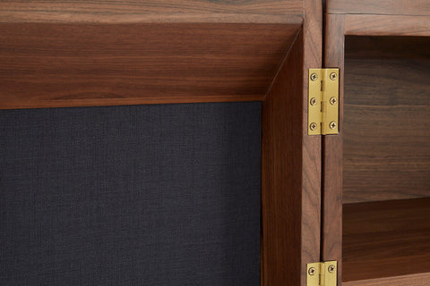 Gold-toned metal hinges on kenso sideboard connect dark wood panels to charcoal fabric backing with deep central drawer