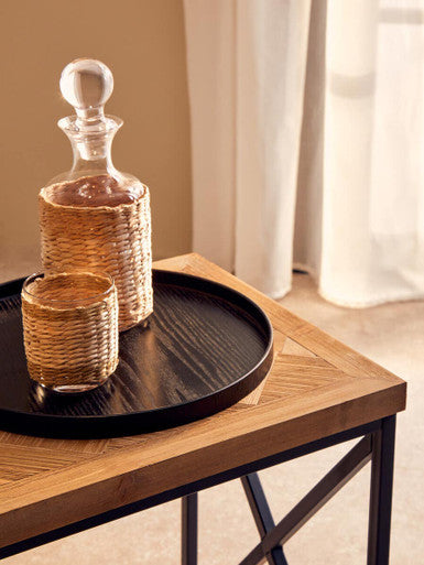 Woven rattan decanter with glass stopper and matching tumbler in natural tan hue on kickford parquet fir wood coffee table