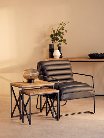 Black leather armchair with sleek metal frame paired with kickford parquet fir wood set of two nesting tables