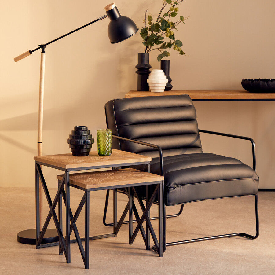Black leather armchair with sleek metal frame next to kickford parquet fir wood set of two nesting tables