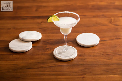 A white marble round coaster with gray veining from the kindia set of 4 marble round coasters under a margarita glass