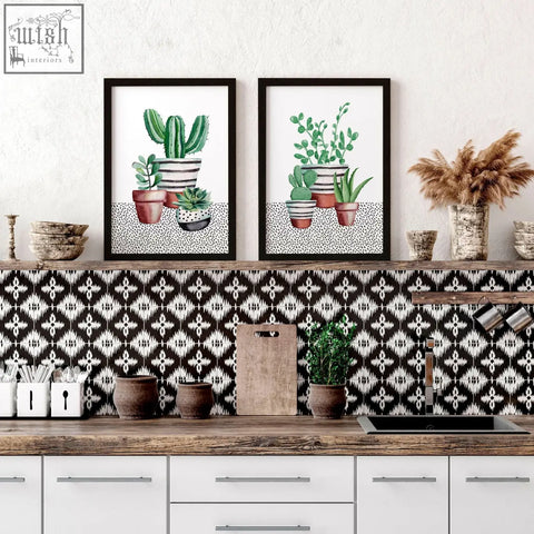Two framed watercolor kitchen prints featuring succulent plants in striped pots above a black and white backsplash
