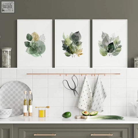 Three framed botanical kitchen wall artwork prints featuring green leaves with gold tones in white frames
