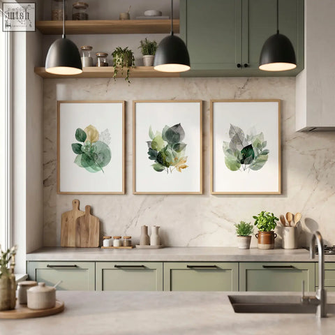 Three framed botanical kitchen wall artwork with watercolor leaves in green and gold tones in light wood frames