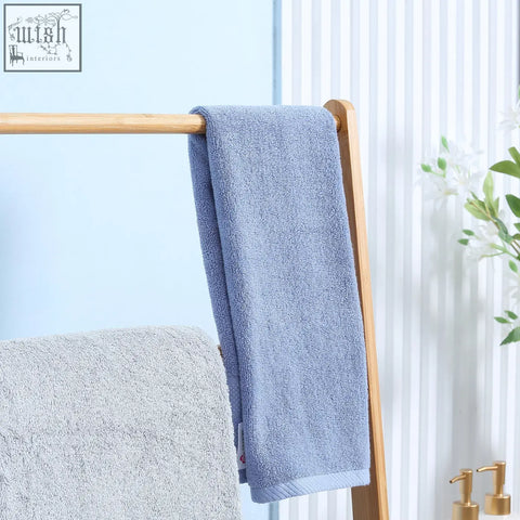 A soft light blue towel hangs on a kleankin freestanding natural bamboo towel rack with three rails and shelves