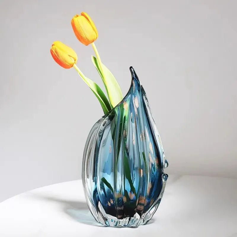 A translucent blue glass kokan vase with vertical ridges and pointed top holding two yellow tulips