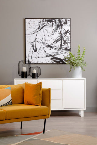 A modern abstract black and white canvas hangs above a sleek white sideboard next to the kolding two seater yellow sofa