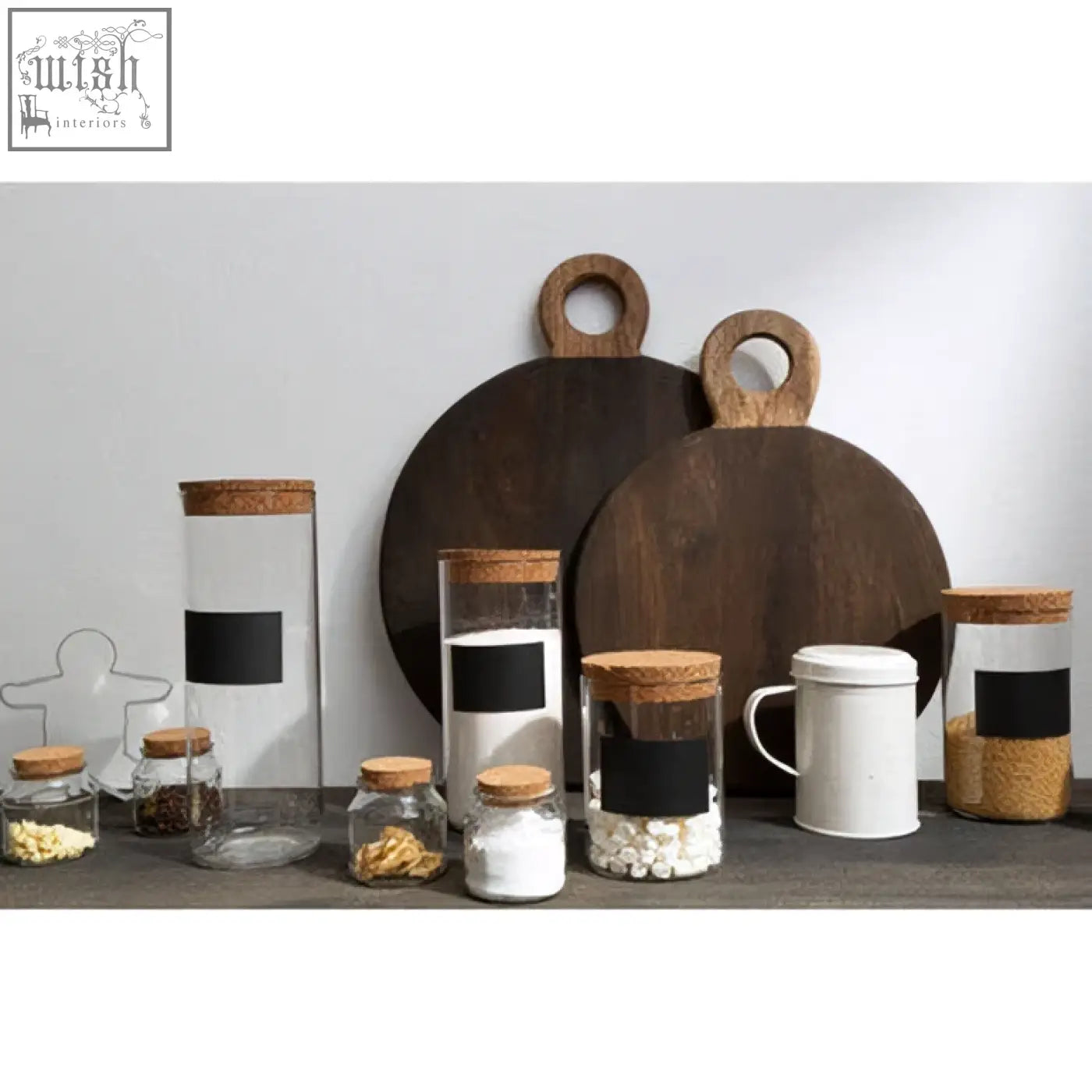 Set of clear glass jars with cork lids next to dark mango wood chopping and serving boards for kitchen use