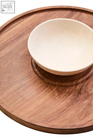 A beige ceramic bowl on a cream marble chip and acacia wood circular chip and dip platter tray