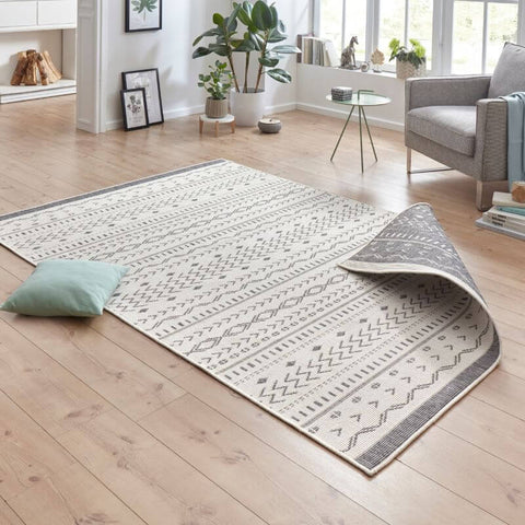 A kuba reversible indoor-outdoor rug with cream base gray geometric patterns and a rolled edge showing textured weave