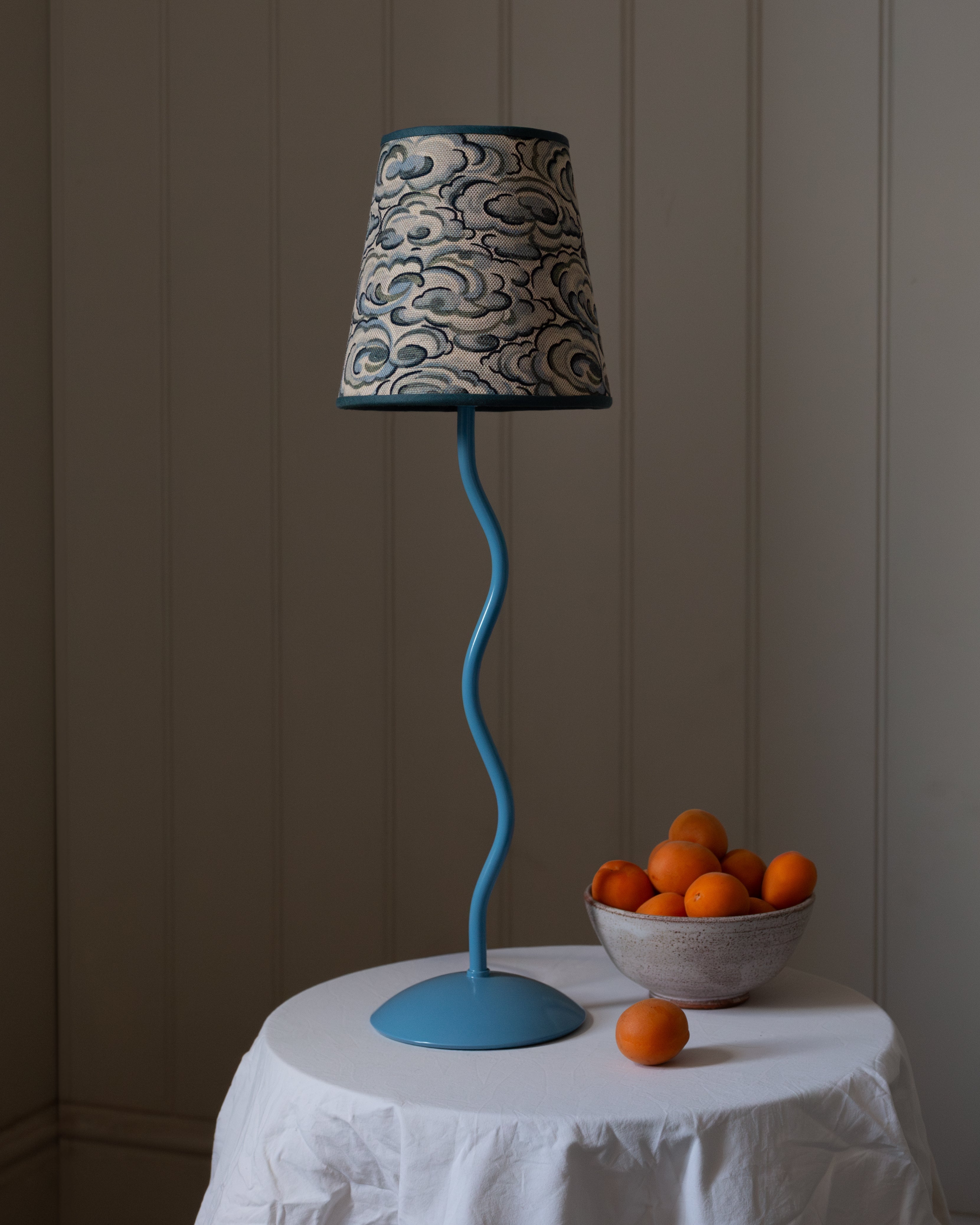 A blue wavy-stem table lamp with a gray and black kumo clouds lampshade featuring an intricate cloud pattern