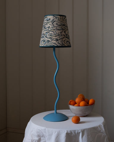 A blue wavy-stem table lamp with a gray and black kumo clouds lampshade featuring an intricate cloud pattern