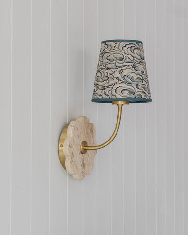 A decorative wall sconce with a brass arm and scalloped stone backplate featuring a kumo clouds lampshade in gray and teal