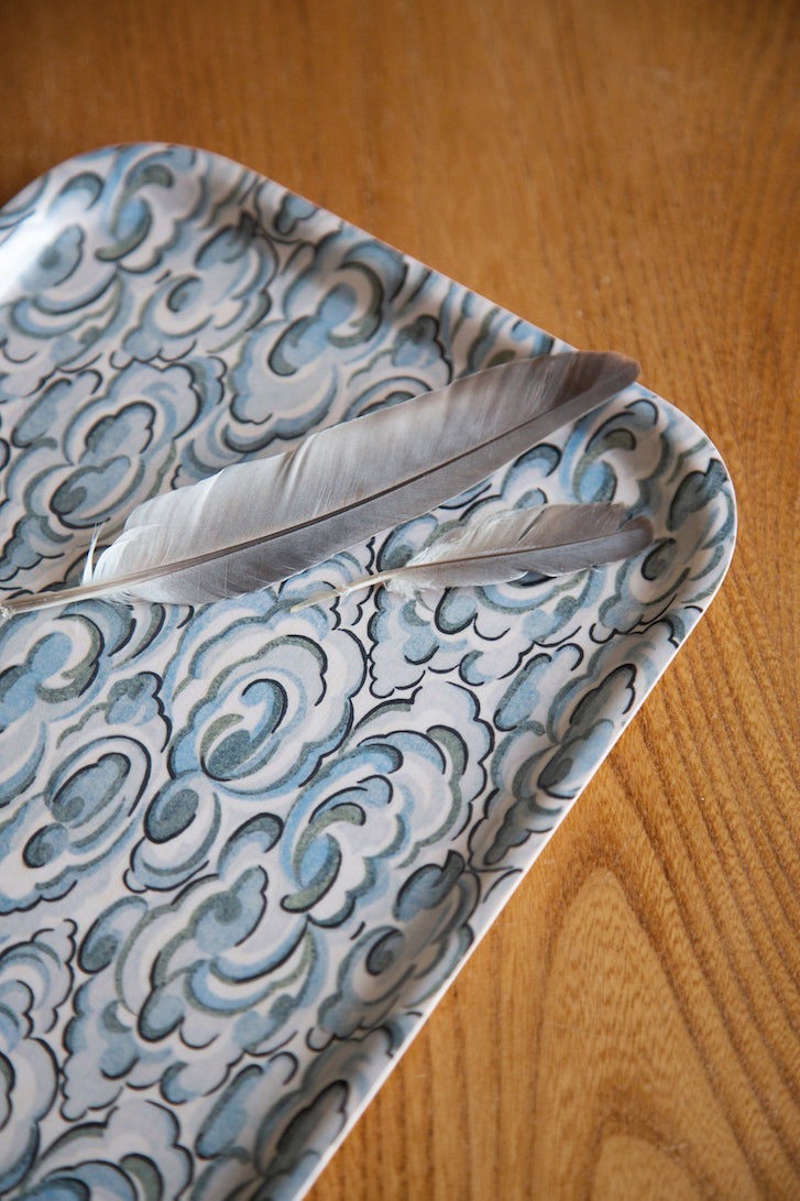 A silver feather on a kumo clouds tray with intricate blue and white cloud pattern in a rectangular shape