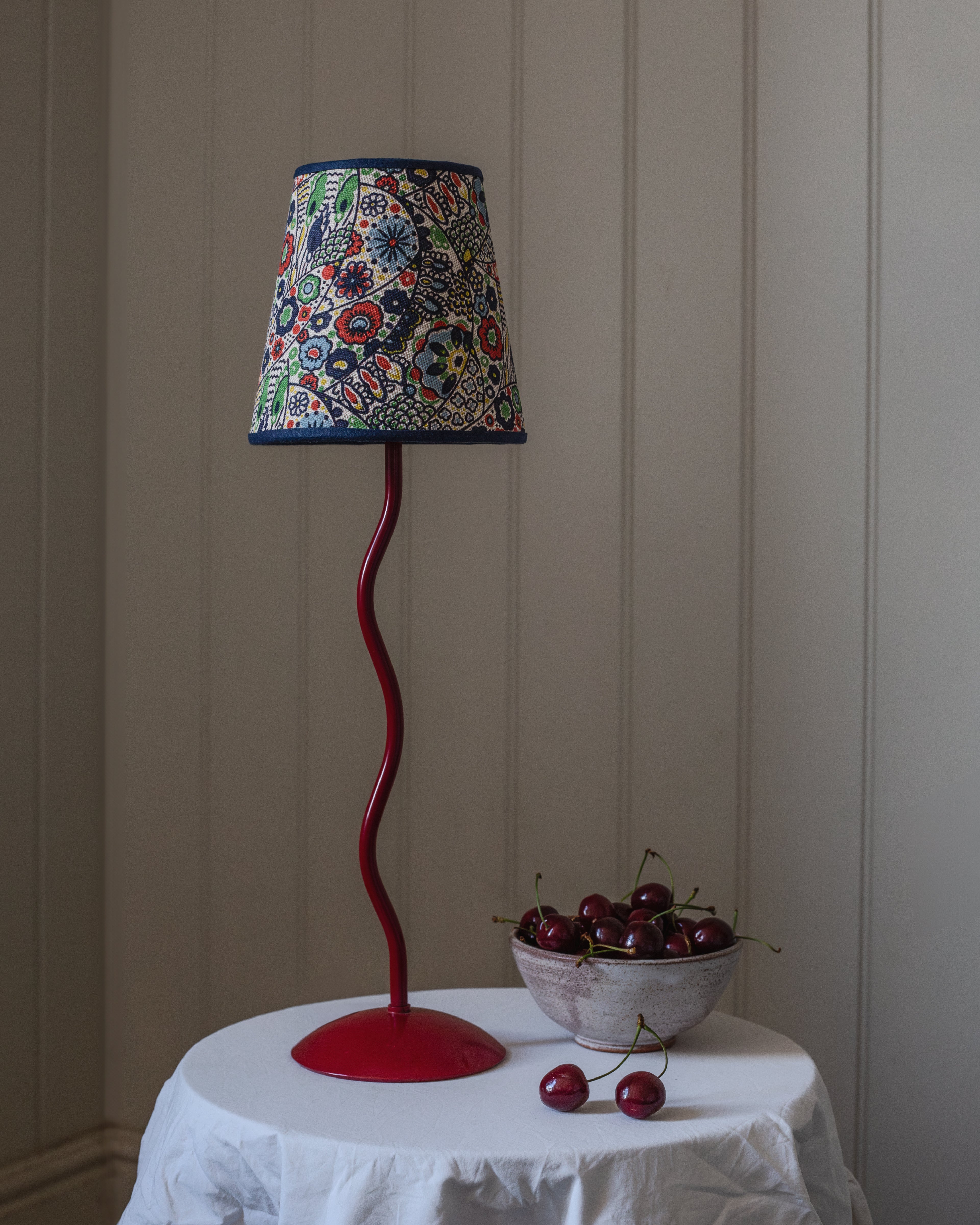 A vibrant red wavy metal base lamp with a colorful floral kyoto woodblock fabric shade and navy blue trim