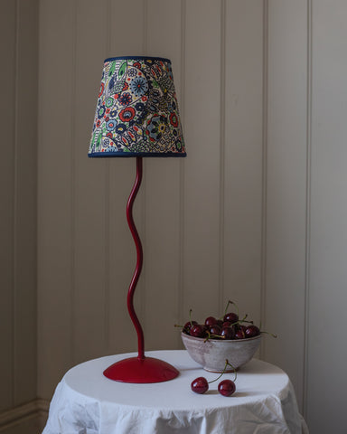 A vibrant red wavy metal base lamp with a colorful floral kyoto woodblock fabric shade and navy blue trim