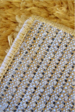 Backside of lagom ochre shaggy rug showing yellow shaggy texture and woven backing with white and black threads
