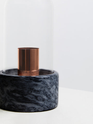 A lamonte bell lamp with a sleek copper cylinder and a black marble base under a clear glass dome