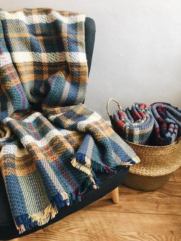 A cozy large checked random recycled wool blanket in multicolored plaid with fringed edges draped over a dark armchair